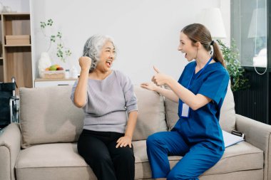 Nurse and older female patient gesturing hands at home. Therapist  taking care of senior woman sitting on sofa. Medical service concept 