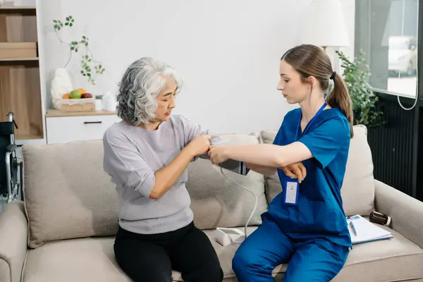 stock image Doctor examining older patient using blood pressure gauge. Therapist at taking care of elderly woman sitting on sofa. Medical service concept