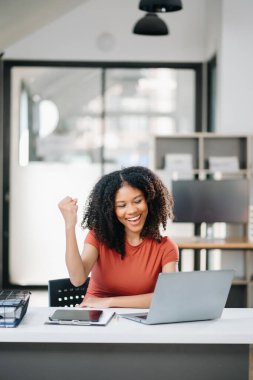 Dizüstü bilgisayar kullanan ve yaratıcı ofiste el kol hareketi yapan genç bir iş kadını.