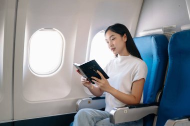 Çekici Asyalı kadın uçak yolcusu İncil okurken rahat koltukta oturuyor. Seyahat biçimi 