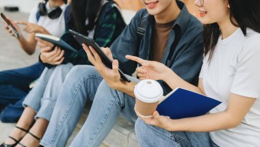 Genç Asyalı üniversite öğrencileri sabah kampüs binasında ders çalışıyor. Birlikte vakit geçirmek, dizüstü bilgisayar ve dijital tablet kullanmak.