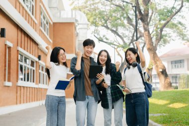Kampüs parkında elinde tablet ve kitaplarla mutlu Asyalı üniversite öğrencileri. 