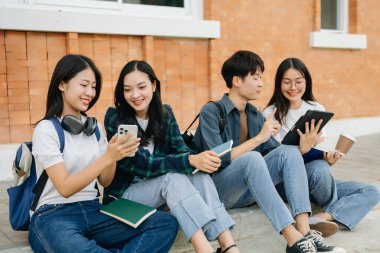 Genç Asyalı üniversite öğrencileri sabah kampüs binasında ders çalışıyor. Birlikte vakit geçirmek, akıllı telefon ve dijital tablet kullanmak.