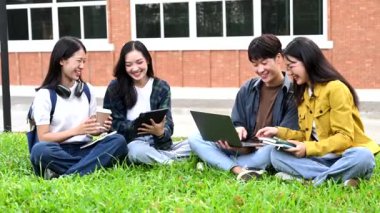 Genç Asyalı üniversite öğrencileri sabah kampüs parkında çimlerin üzerinde otururken ders çalışıyorlar. Birlikte vakit geçirmek, dizüstü bilgisayar ve dijital tablet kullanmak.