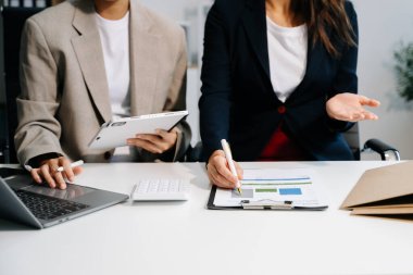 Ofisteki yeni projeyi tartışan ve çalışan meslektaşlar dizüstü bilgisayar ve dijital tablet kullanıyorlar 