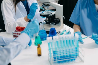 Bir tıp laboratuvarında araştırma yapan takım bilim adamları, ön plandaki bir araştırmacı, tıp laboratuarında bir mikroskop kullanıyor.. 