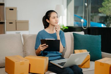 Başlangıçta küçük işletme KOBİ 'si, dizüstü bilgisayar kullanan girişimci kadın, ürün kutularını hazırlamak için online alışveriş siparişi alıyor ve kontrol ediyor 
