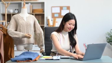  Moda tasarımcısının masasında dizüstü bilgisayar kullanan Asyalı genç bir kadın. 