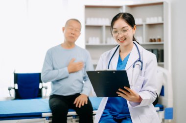 Beyaz takım elbiseli Asyalı doktor, hastanede ya da klinikte salin solüsyonu alan Asyalı yaşlıları ve yatakta yatan hastaları tartışırken not alıyor.