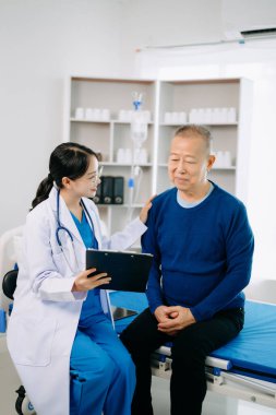 Beyaz takım elbiseli Asyalı doktor, hastanede ya da klinikte salin solüsyonu alan Asyalı yaşlıları ve yatakta yatan hastaları tartışırken not alıyor.