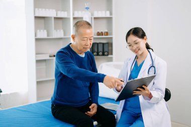 Beyaz takım elbiseli Asyalı doktor, hastanede ya da klinikte salin solüsyonu alan Asyalı yaşlıları ve yatakta yatan hastaları tartışırken not alıyor.