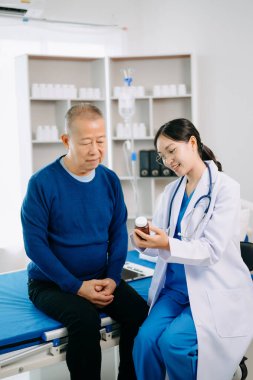 Beyaz takım elbiseli Asyalı doktor, Asyalı yaşlılara ilaç alıyor. Hastanede ya da klinikte salin solüsyonu alan bir hasta.