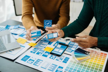  UX geliştiricisi ve ui tasarımcısı modern ofis müşteri özeti ve renk kodlu mobil uygulama arayüzü kablo dizaynı, dizüstü bilgisayar ve telefon hakkında beyin fırtınası yapıyorlar.