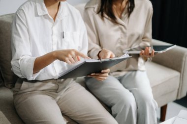 İki genç iş adamı akıllı telefondan konuşuyor ve ofisteki kanepede dizüstü bilgisayar kullanıyorlar.