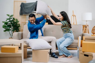 Büyük kutuları olan genç bir çift yeni bir eve taşınıyor. Yastıklarla kavga ediyorlar. 