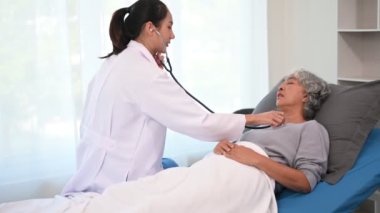 Genç doktor yatakta yatan yaşlı kadın hastayla konuşuyor.