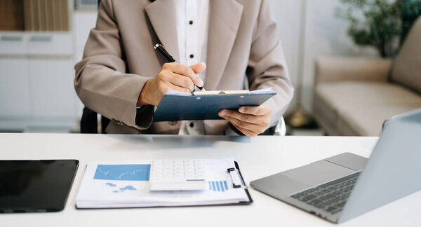 Confident businessman working on clipboard and laptop on the workplace at modern office