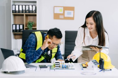 Miğferler, planlar, ev modelleri ve dizüstü bilgisayarlarla birlikte çalışan Asyalı mühendisler. Modern ofiste Asya endüstrisi profesyonel takımı.