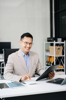 Asyalı işadamı çalıştığı yerde bilgisayarını ve tabletini kullanıyor..