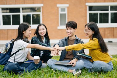 Genç Asyalı kolej öğrencileri sabahları çimde otururken kampüs parkında el ele tutuşuyorlar. Birlikte vakit geçirmek.