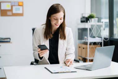 Akıllı telefon, dizüstü bilgisayarla çalışan ve yaratıcı ofisteki masada not alan kendine güvenen bir iş uzmanı. 