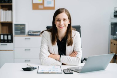 Kendine güvenen bir iş uzmanı dizüstü bilgisayarla çalışıyor ve yaratıcı ofisteki kameraya bakıyor.