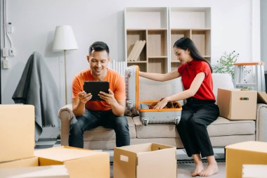 Happy asian young attractive couple man and woman with big boxes moving into a new house and using digital tablet  clipart