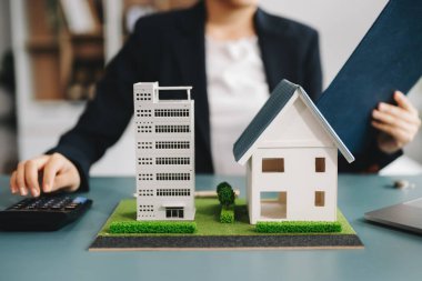 Emlak komisyoncusu ev modelini sunar. İş kadını, ofisteki ipotek kredisi teklifiyle ilgili müşteriye danışıyor 