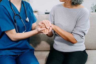 Genç hemşire yaşlı kadına yardım ediyor, el ele tutuşuyor, destek oluyor. Destekli yaşam tesisinde yaralanma üstüne tedavi ve rehabilitasyon