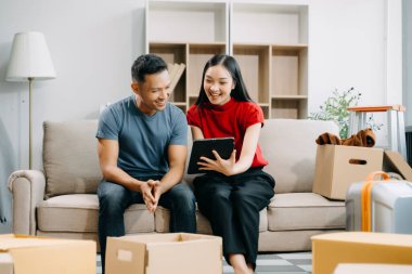 Asyalı genç ve çekici bir çift, yeni evi dekore etmek için online alışveriş mobilyaları için tablet kullanıyor. Genç evli Asyalı yeni evine taşınıyor.