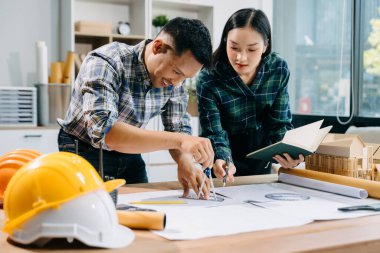 Asyalı mühendisler miğferler, planlar ve ofis modelleriyle birlikte mimarlık projesinde birlikte çalışıyorlar.. 