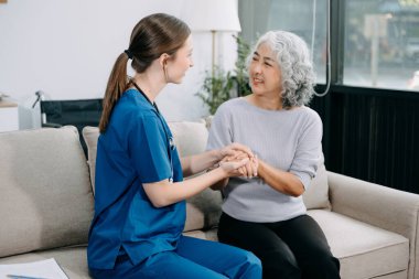 Genç hemşire yaşlı kadına yardım ediyor, el ele tutuşuyor, destek oluyor. Destekli yaşam tesisinde yaralanma üstüne tedavi ve rehabilitasyon