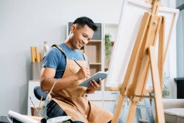 Asyalı erkek ressam sanat atölyesinde resim yapıyor, resim malzemeleri, yağ rengi, tuval sehpası, sanat atölyesinde yaratıcı alan