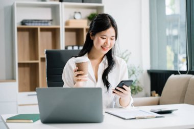 Ofiste çalışmak için akıllı telefon dizüstü bilgisayarı kullanan çekici bir iş kadını.  