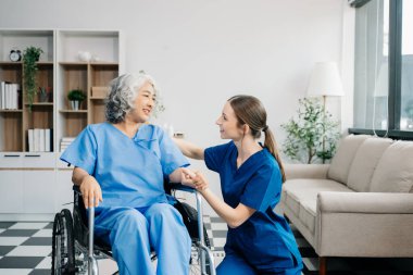 Young nurse helping elderly woman  in the room, holding her hand, supporting. Treatment and rehabilitation after injury in assisted living facility, senior care