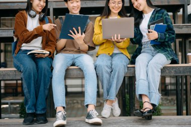 Genç Asyalı üniversite öğrencileri sabahleyin kampüs parkında ders çalışıyor. Birlikte vakit geçirmek, dizüstü bilgisayar kullanmak. 