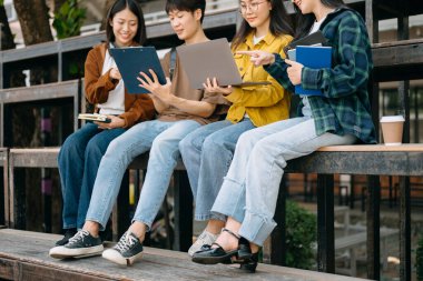 Genç Asyalı üniversite öğrencileri sabahleyin kampüs parkında ders çalışıyor. Birlikte vakit geçirmek, dizüstü bilgisayar kullanmak. 
