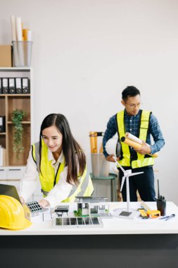 Mimari proje sahasında çalışan mühendis ekibi ve modern ofiste yeşil enerjili model ev yapıyorlar.  