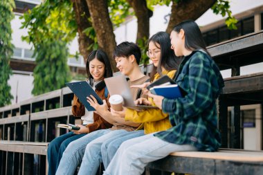 Genç Asyalı üniversite öğrencileri sabahleyin kampüs parkında ders çalışıyor. Birlikte vakit geçirmek, dizüstü bilgisayar kullanmak.