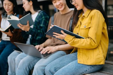 Genç Asyalı üniversite öğrencileri sabahleyin kampüs parkında ders çalışıyor. Birlikte vakit geçirmek, dizüstü bilgisayar kullanmak. 