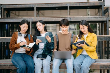 Genç Asyalı üniversite öğrencileri sabahleyin kampüs parkında ders çalışıyor. Birlikte vakit geçirmek, dizüstü bilgisayar ve dijital tablet kullanmak.