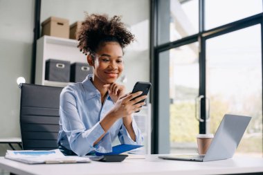 Yaratıcı ofisteki masada akıllı telefon kullanan genç bir iş kadını.