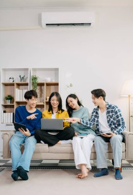 Dijital tabletli dizüstü bilgisayar ve evde online bilgi kullanarak proje ödevi üzerinde çalışan bir grup Asyalı genç üniversite öğrencisi 