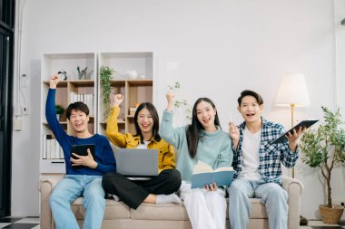 Dijital tabletli dizüstü bilgisayar ve evde online bilgi kullanarak proje ödevi üzerinde çalışan bir grup Asyalı genç üniversite öğrencisi 