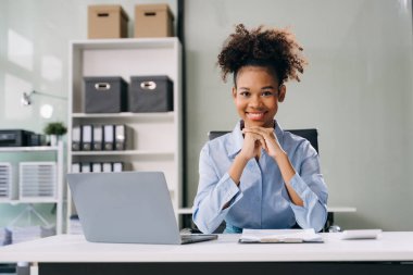 Genç ve güzel bir kadın iş yerinde kameraya poz verirken dizüstü bilgisayar kullanıyor.