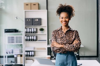 Modern ofisteki Afrikalı iş kadını ellerini çapraz yaparak masada duruyor. 