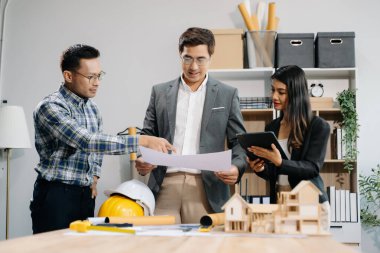 Mühendis takımları mimari proje sahasında birlikte çalışarak model ev yapıyorlar. Modern ofiste Asya endüstrisi profesyonel takımı