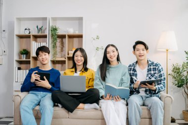 Dijital tabletli dizüstü bilgisayar ve evde online bilgi kullanarak proje ödevi üzerinde çalışan bir grup Asyalı genç üniversite öğrencisi 
