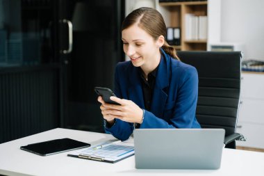 Yaratıcı ofiste masa başında otururken akıllı telefon kullanan kendine güvenen bir iş kadını.