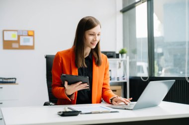 Ofisteki masada dizüstü bilgisayar ve dijital tablet kullanan iş kadını